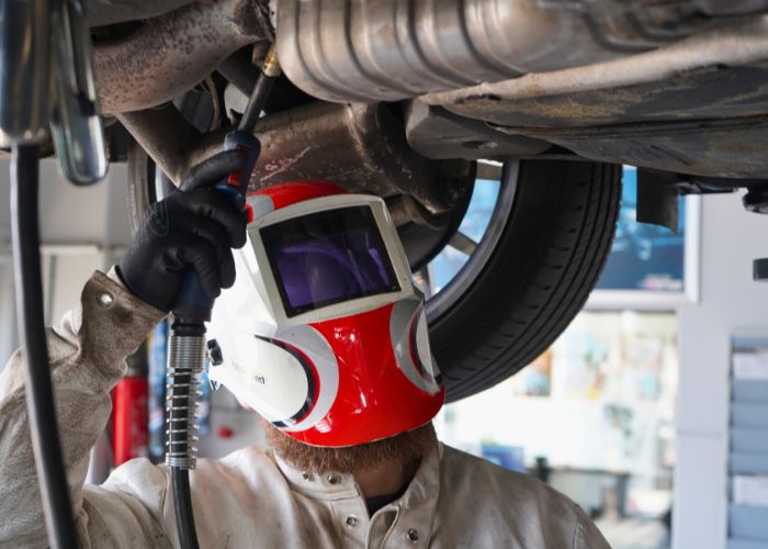 kfz_hildebrand-auspuffsystem_abgasanlage-700x500 Werkstatt Mitarbeiter schweißt an der Auspuffanlage unter einem Fahrzeug.