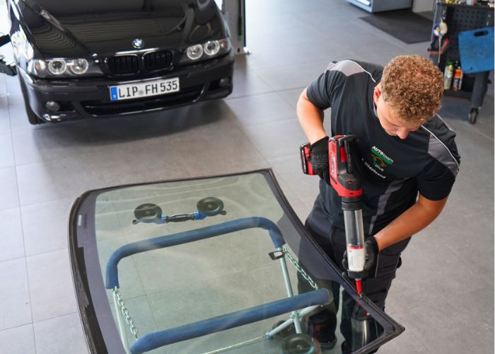 kfz_hildebrand-autoglasreparatur-700x500 Werkstatt Mitarbeiter wechselt Frontscheibe an einem Fahrzeug.