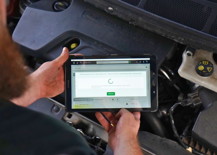 kfz_hildebrand-motordiagnose_und_fehlerdiagnose-700x500 Werkstatt Mitarbeiter führt eine Motordiagnose an einem Fahrzeug aus und hält dabei ein Tablet in der Hand.