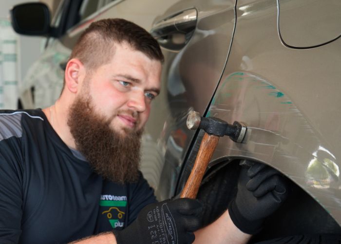 kfz_hildebrand-reparatur_und_instandsetzung-700x500 Werkstatt Mitarbeiter repariert Karosserie von einem Fahrzeug.